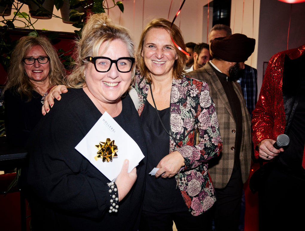 Margit Stolzlechner und ein Gast halten ein Gutschein für die Hollerei.